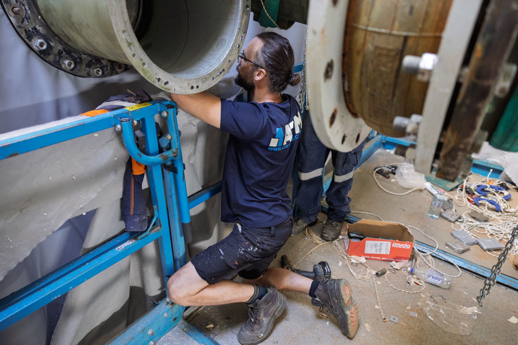 ATM Tanks — A worker kneeling on a scissor lift platform, fitting a pipe section by hand